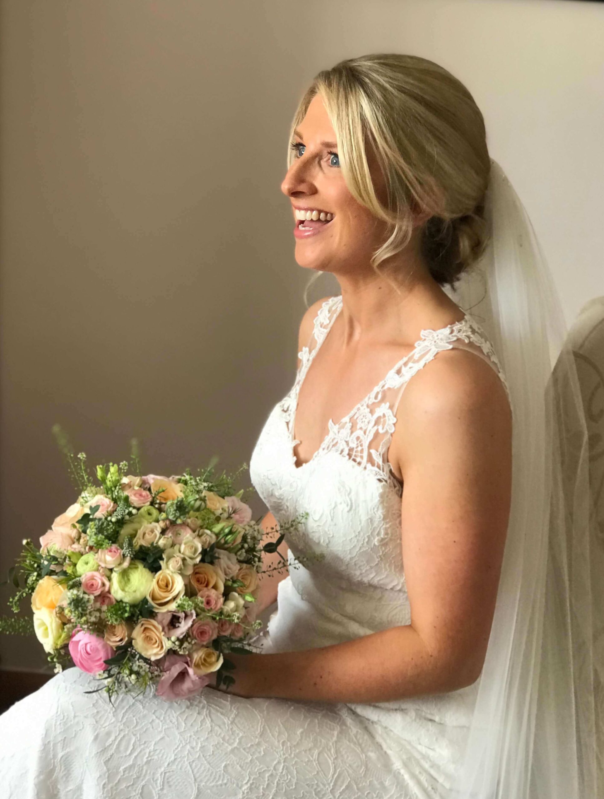 smiling blonde bride with hair pinned up with long veil subtle natural makeup, rose bouquet with butterflies